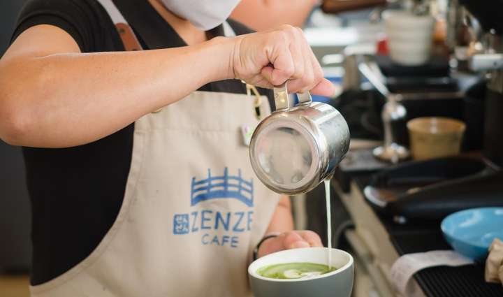 an image of zezen cafe barista pooring milk over a matcha latte